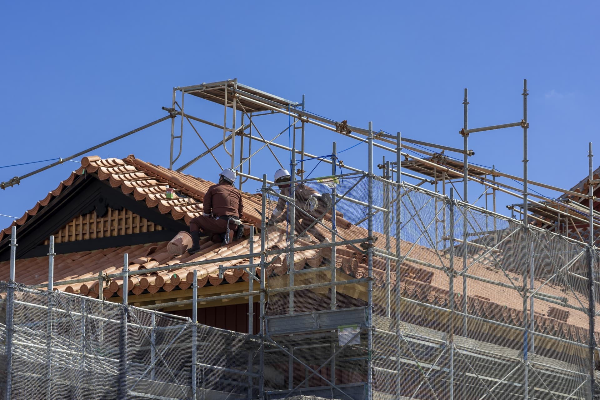 足場を設置して瓦屋根の葺き替え工事を行う職人の作業風景