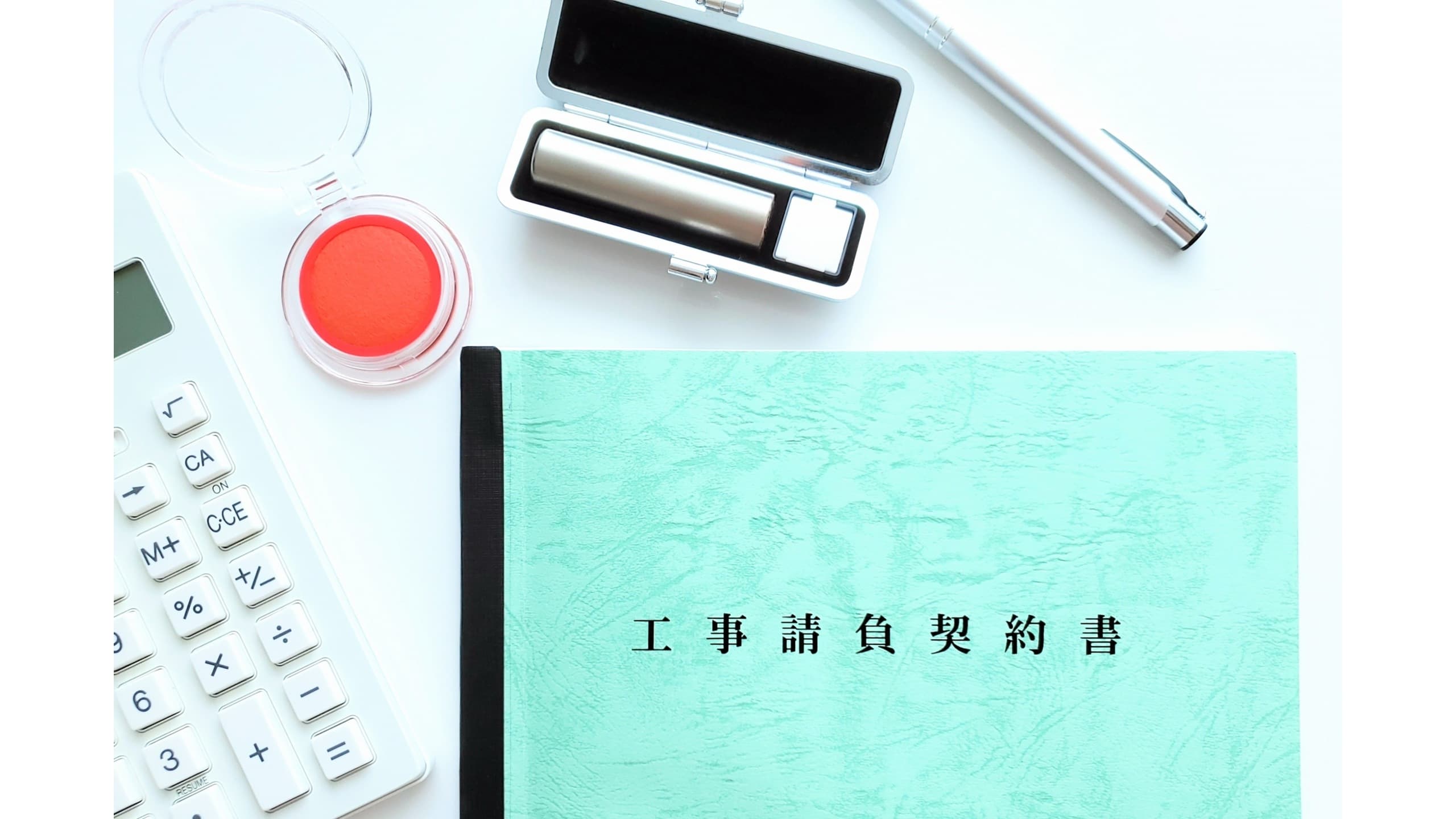 工事請負契約書の表紙と印鑑、計算機が並ぶ契約手続きのイメージ